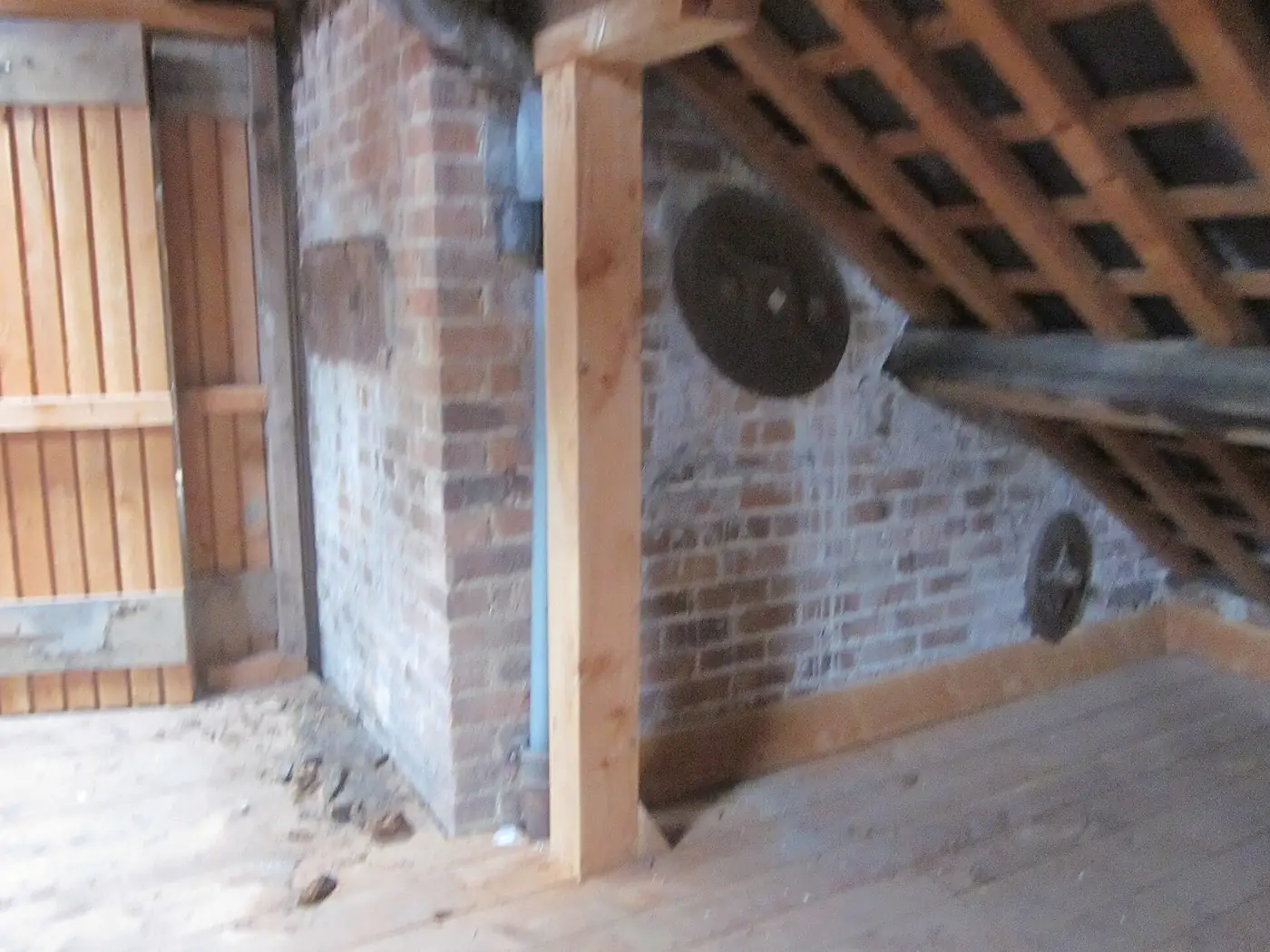 The inside of a farm building with exposed timber roof beams, brick walls and a wooden door