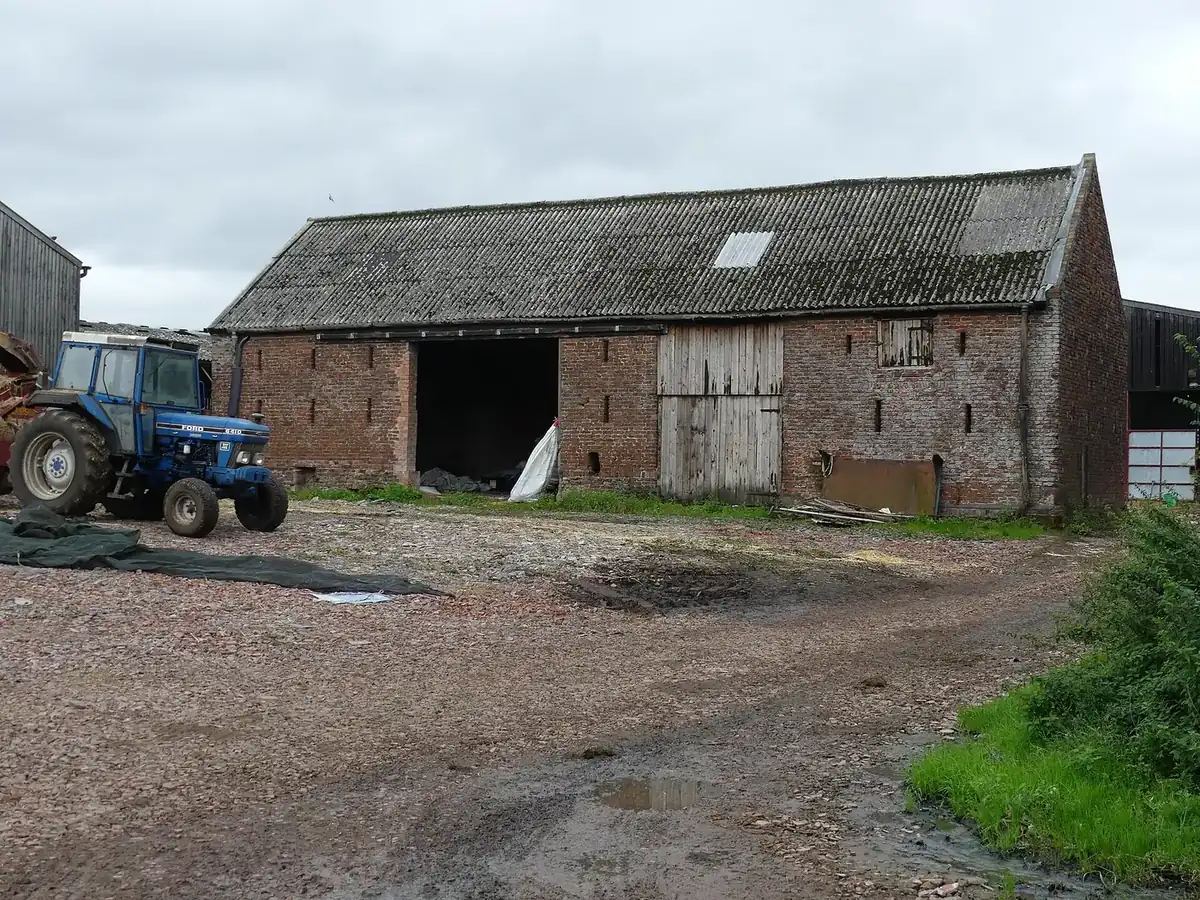 A brick and timber farm barn with a tractor parked in front, beside other farm buildings