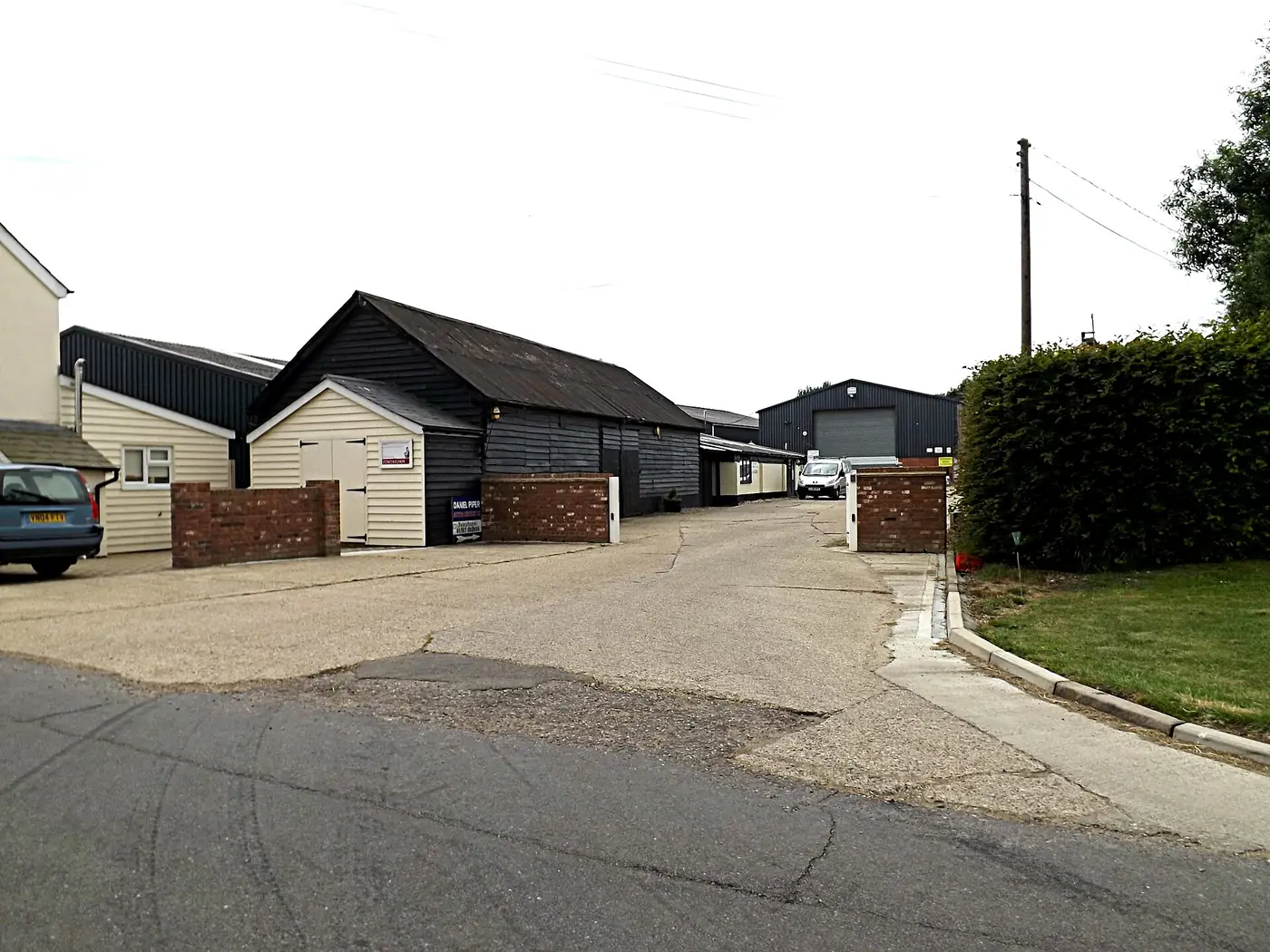 A row of black timber farm buildings converted into business units, with cars parked in the yard