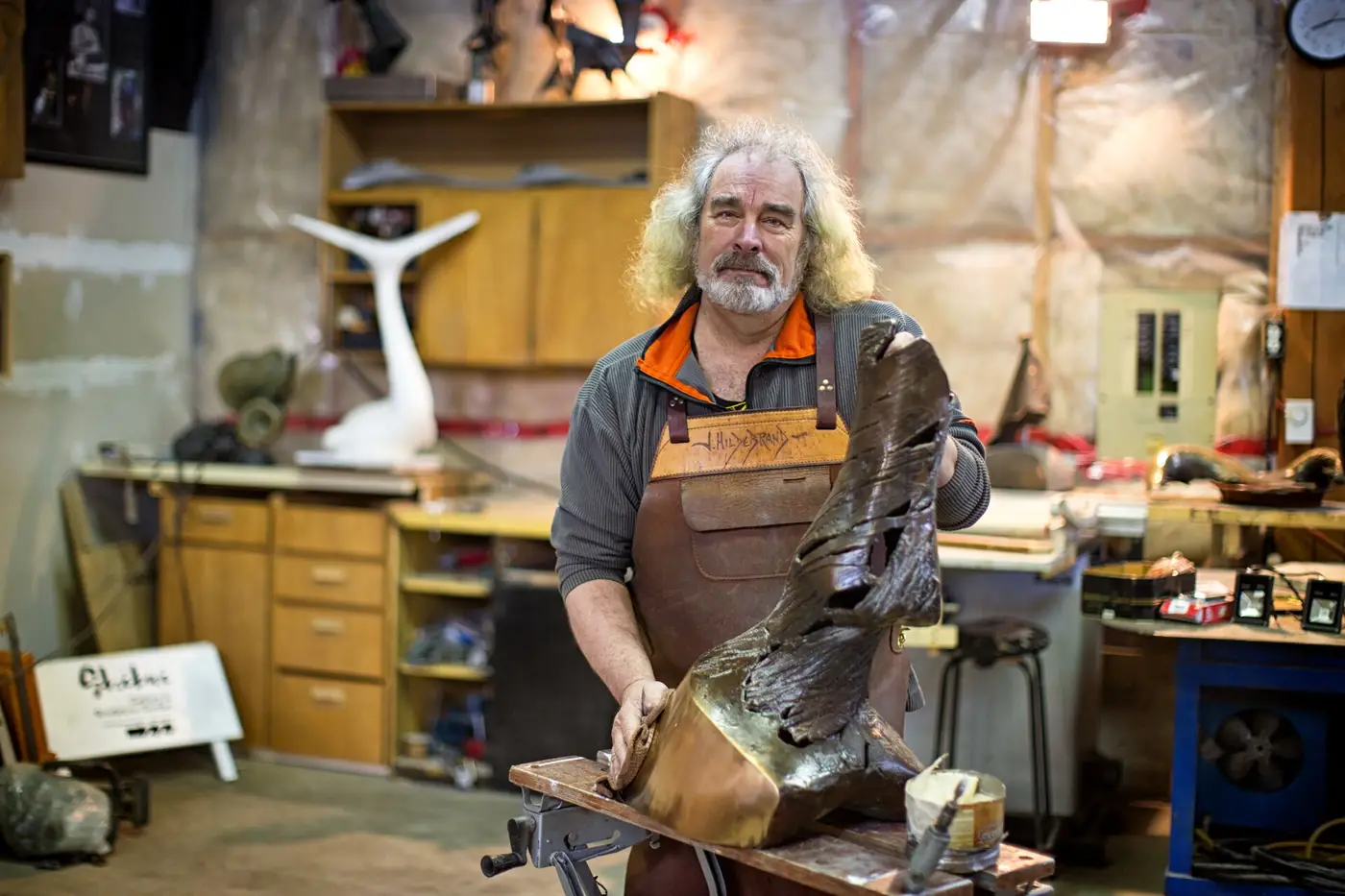 A craftsman shaping wood in a workshop surrounded by tools and workbenches
