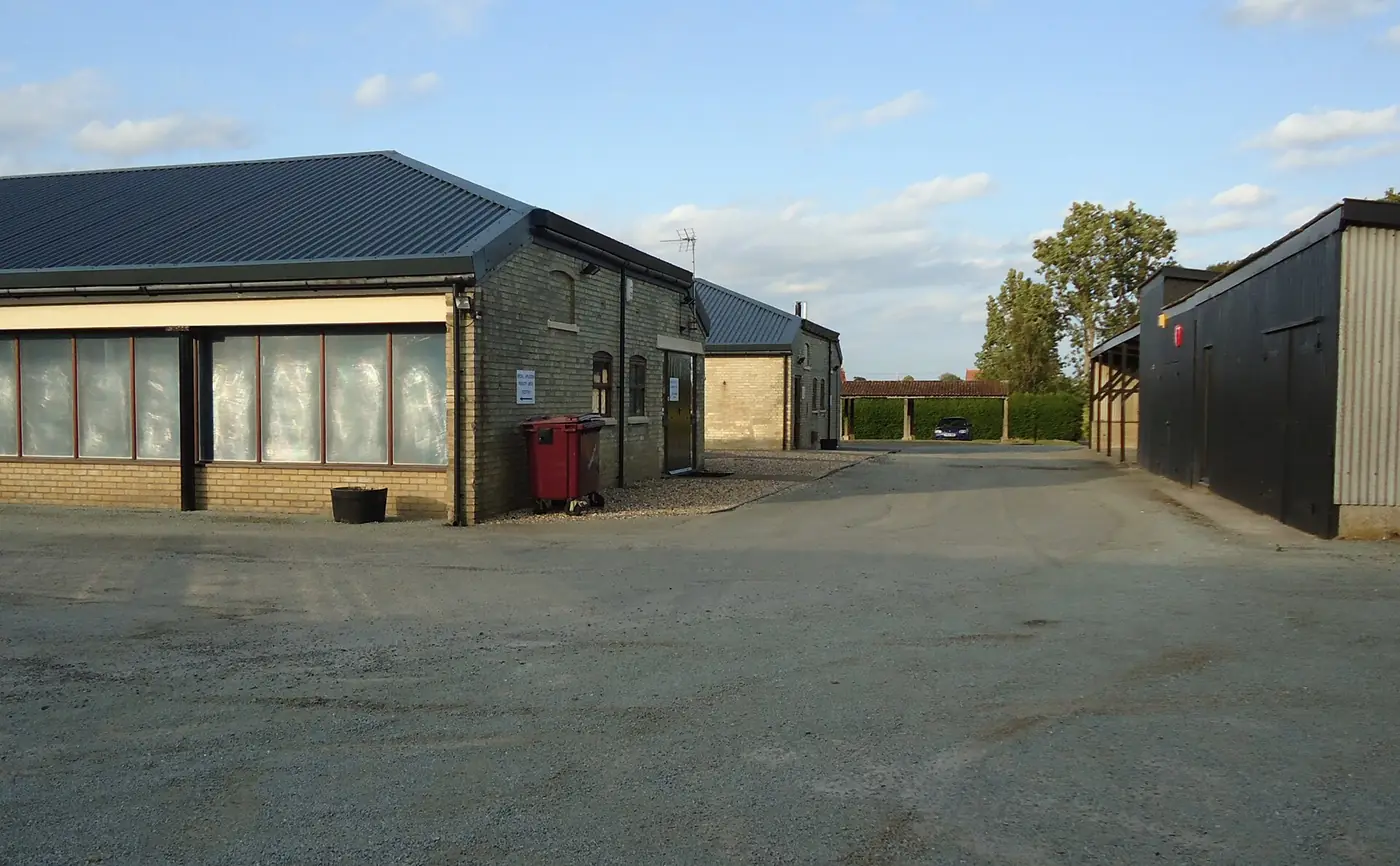 Converted farm buildings around a yard with parked vans and cars
