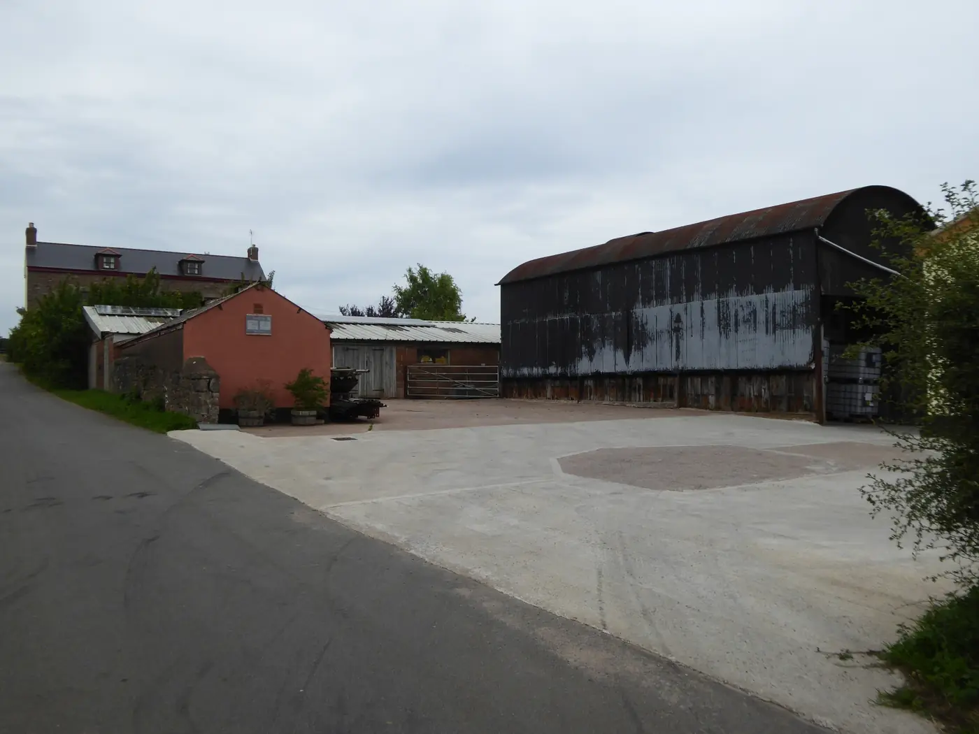 A traditional farmyard with a large black timber barn and brick buildings around a concrete yard