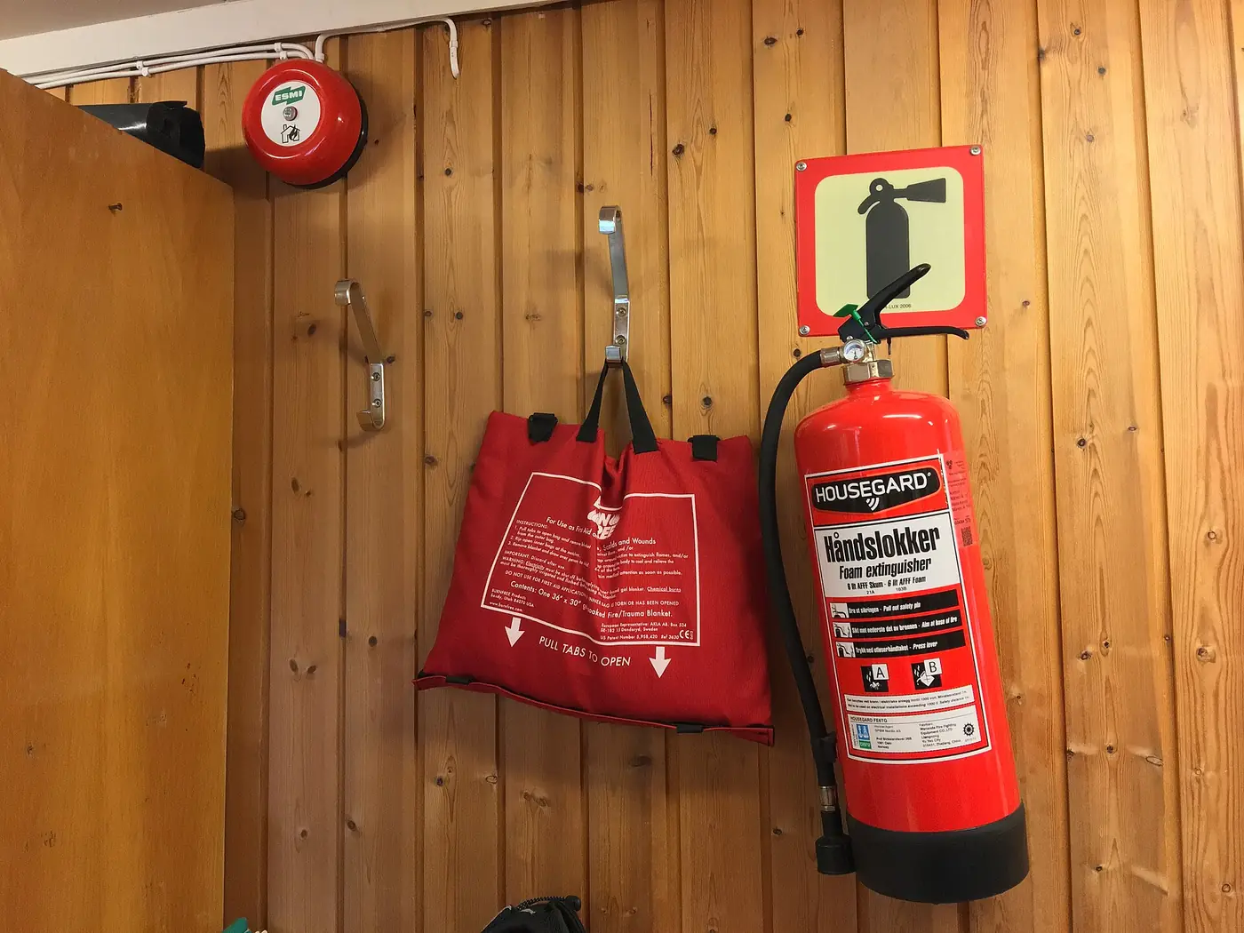 A red foam fire extinguisher and a fire blanket mounted on a timber-clad wall