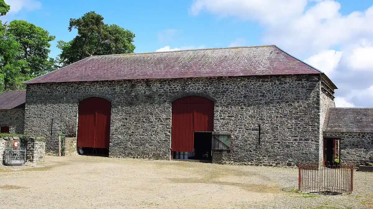 A long flint and brick threshing barn with two large red doors facing a gravel yard