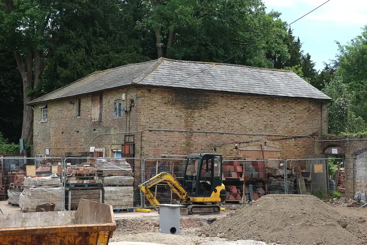 A former builders yard with a stone barn, stacked materials and a small excavator