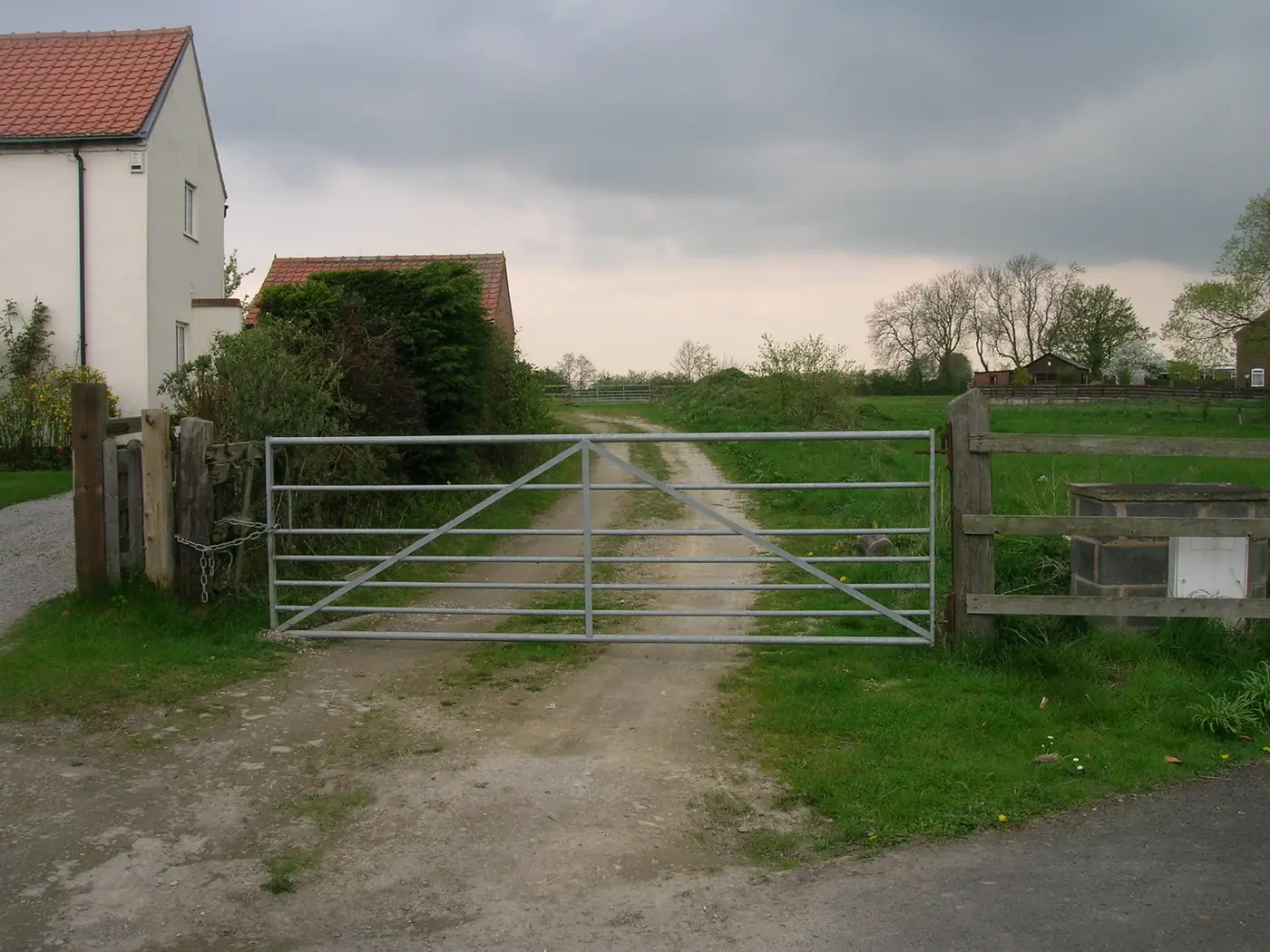 A metal farm gate across a gravel track leading to farm buildings
