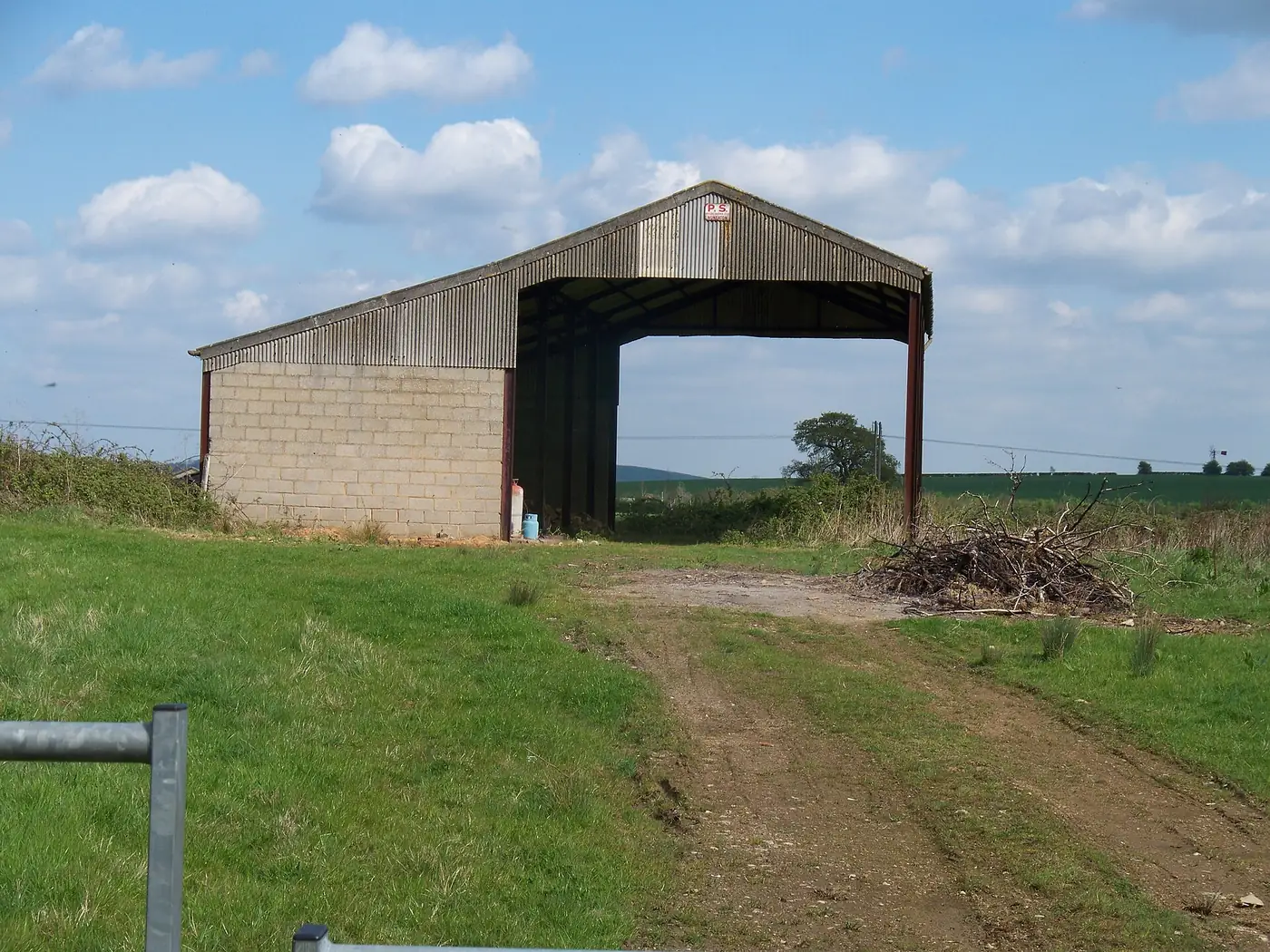 A large open-fronted farm barn of blockwork and steel cladding beside a grassy track