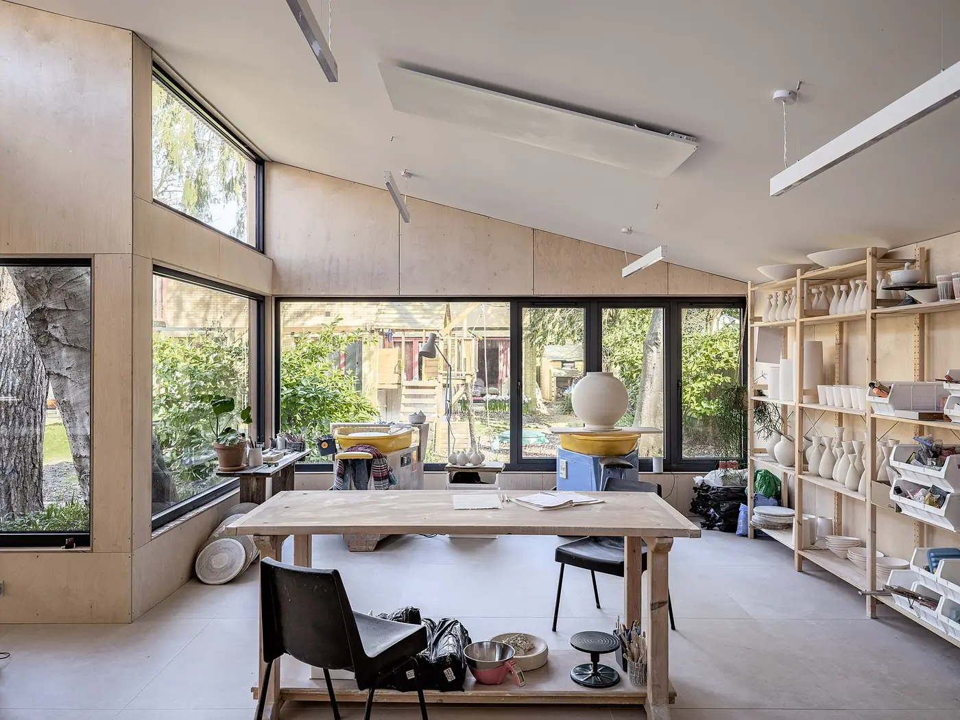 A bright pottery studio with large windows, a workbench and shelves of ceramics