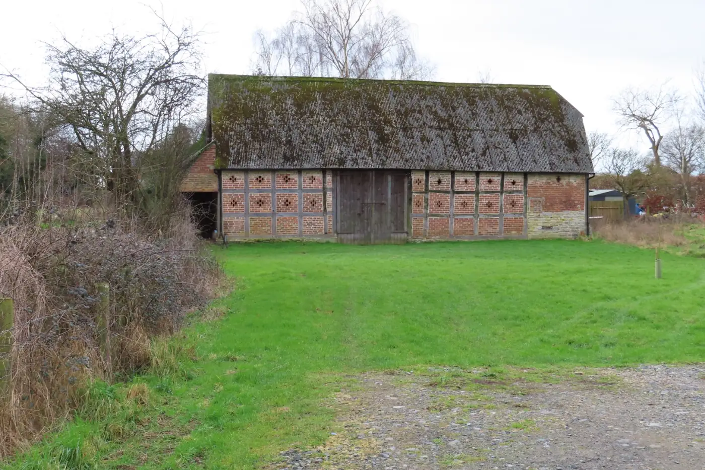 A long timber-framed barn with a tiled roof in a grassy farmyard