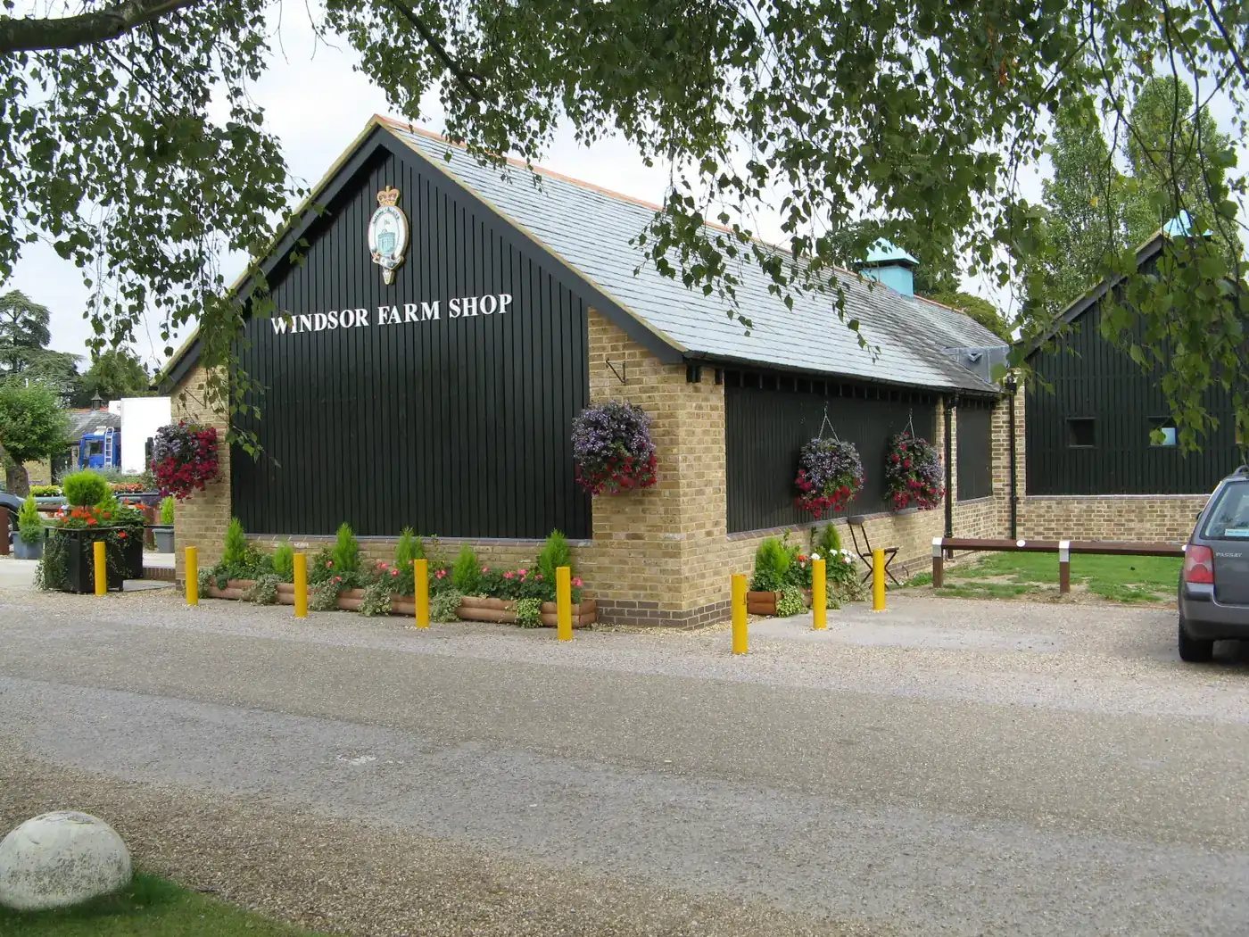 A black timber farm shop building with a gravel forecourt and hanging baskets